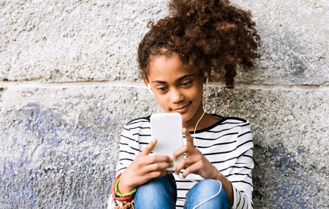 young girl in striped shirt with ponytail and headphones reading phone