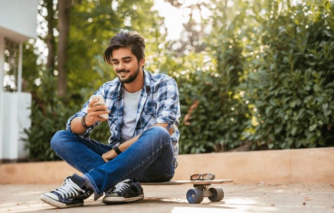 teenager reading on phone with skateboard outside