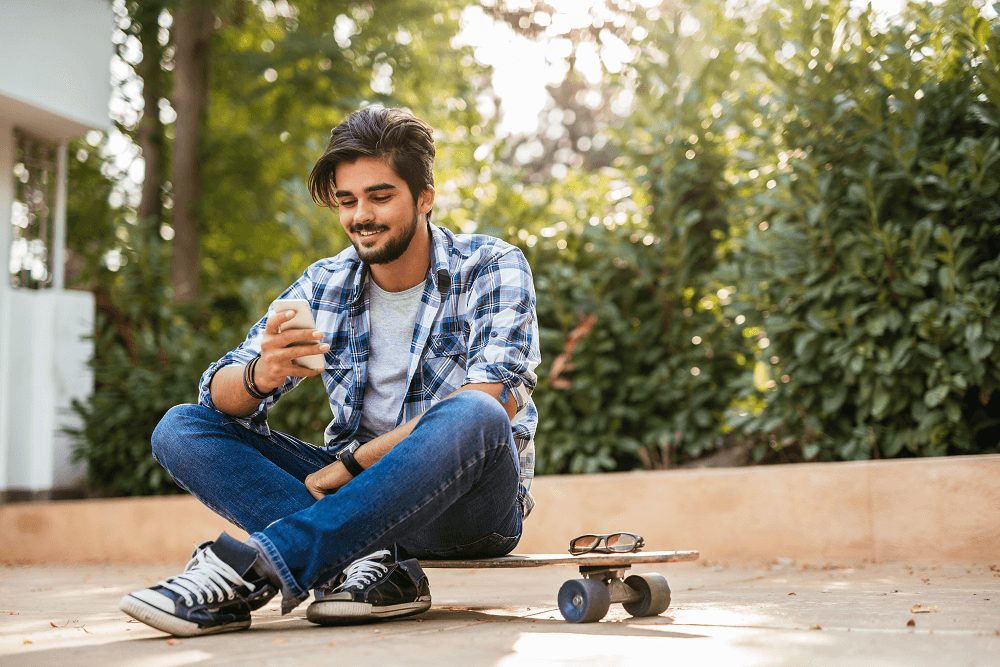 teenager reading on phone with skateboard outside