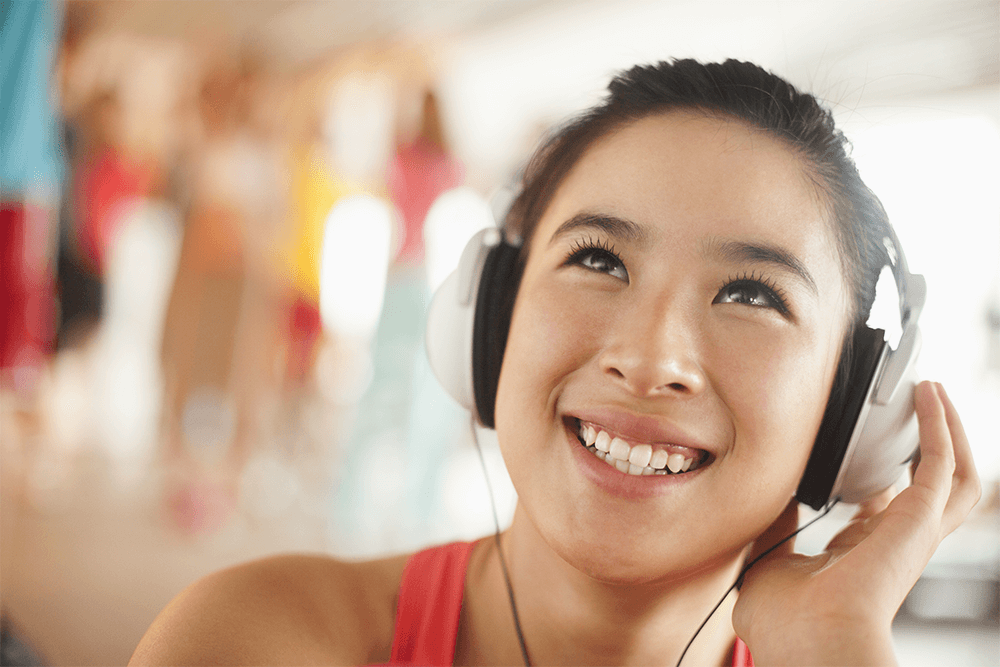 sync audiobooks for teens blog feature image: happy teenage girl smiling and using over-the-ear headphones