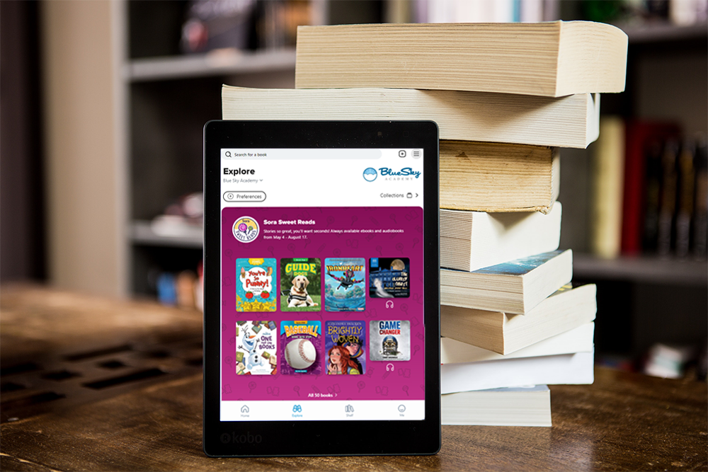 using sora side-by-side with your physical library: a tablet with the Sora home screen resting against a pile of paperback books