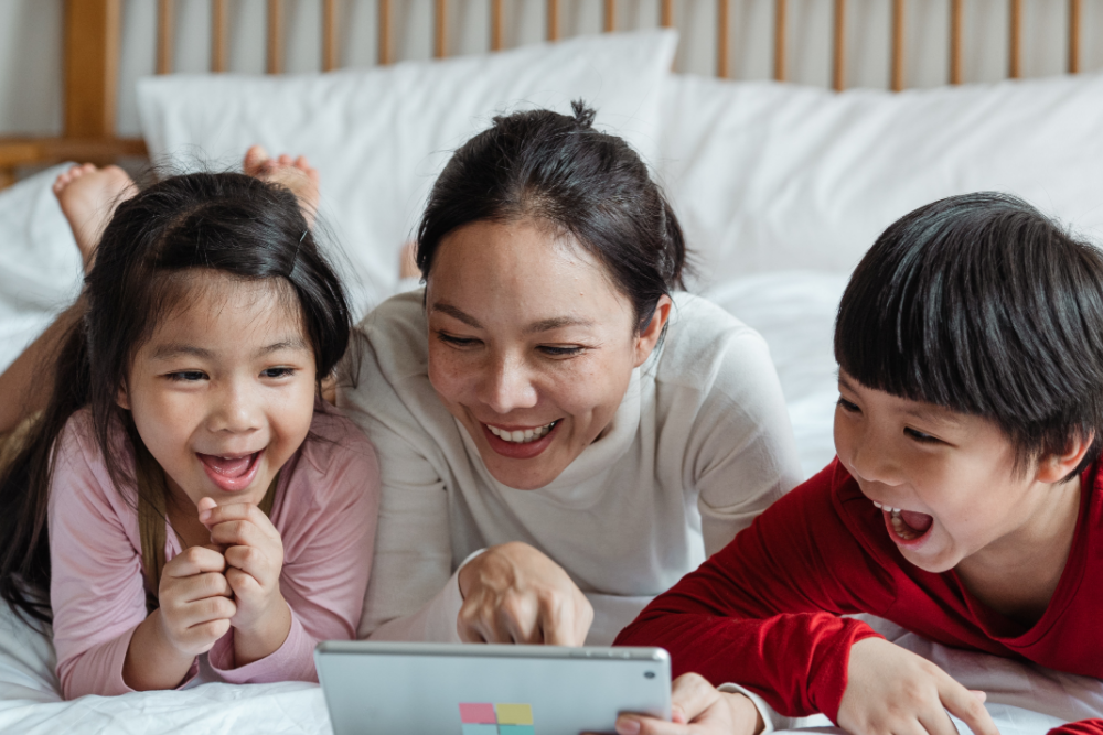 An Asian mother and her two children enjoy an ebook from Children Bilingual Books
