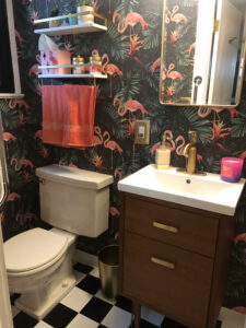 Photo of a small guest bathroom with green and pink Flamingo wallpaper, black and white checkered floor, and a mid century modern inspired wood vanity sink with gold accents